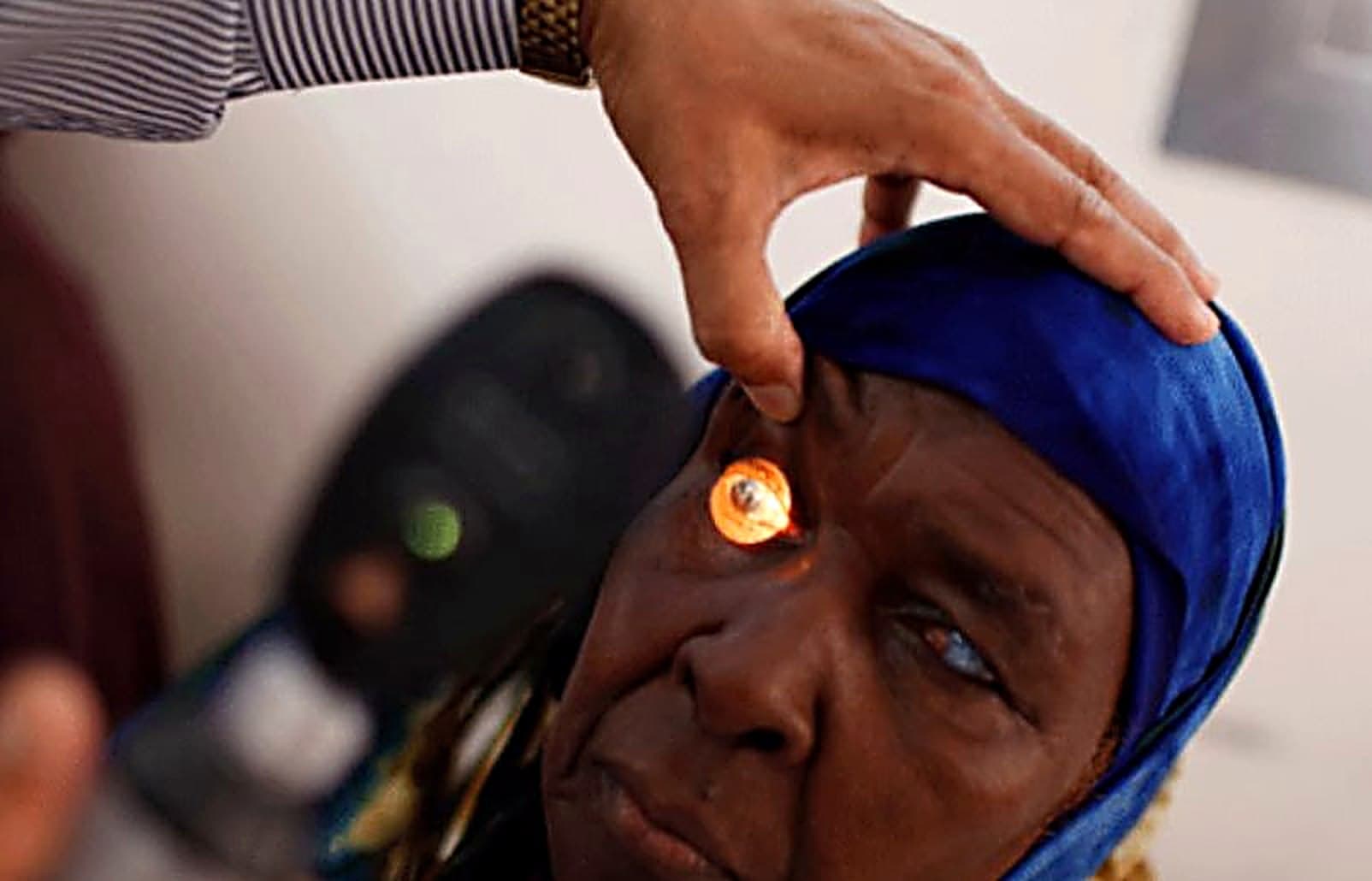 A God First Eye Specialist Hospital clinician gently examining an elderly patient's eye with a penlight